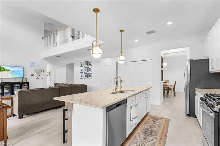 Kitchen with white cabinetry, stainless steel dishwasher, light stone countertops, a breakfast bar, and a kitchen island with sink