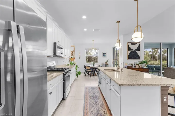 Kitchen featuring appliances with stainless steel finishes, white cabinets, recessed lighting, light stone countertops, and a center island with sink