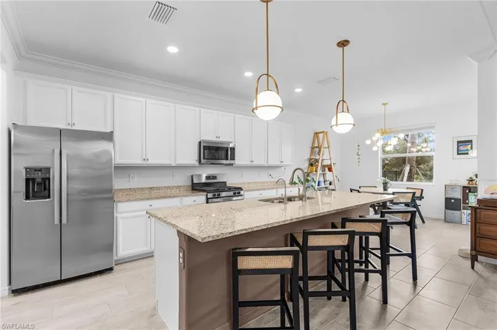 Kitchen with stainless steel appliances, crown molding, white cabinetry, a breakfast bar area, and an island with sink