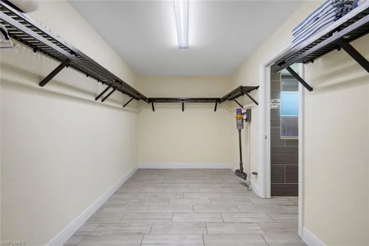 Spacious closet featuring wall-mounted shelving, wood-finish tile flooring, a white trim baseboard, and ceiling-mounted lighting