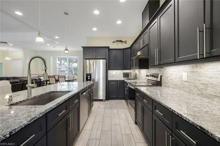 Modern kitchen featuring dark cabinetry, stainless steel appliances, and a central island with a built-in sink
