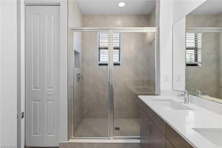 Full bath featuring a closet, a shower stall, double vanity, and plenty of natural light