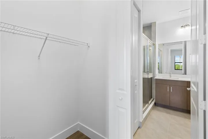 Full bath with a shower stall, vanity, a walk in closet, and light tile patterned floors