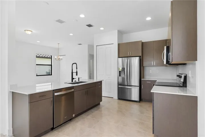 Kitchen featuring stainless steel appliances, suspended lighting, light stone countertops, light tile patterned floors, and dark wood finish cabinets