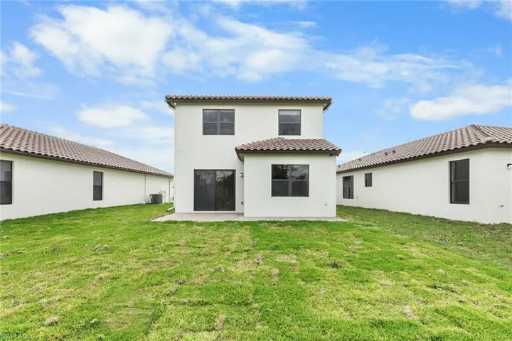 Rear view of property with a lawn, stucco siding, a tiled roof, and a patio area