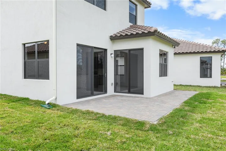 Back of house featuring a lawn, a patio area, stucco siding, and a tiled roof