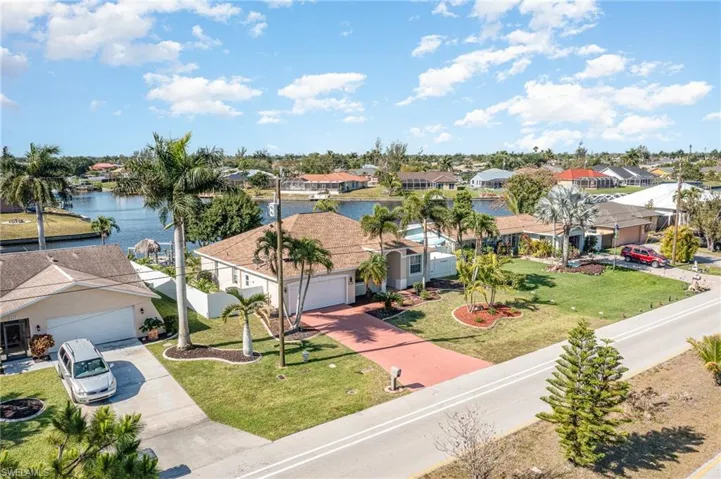 Waterfront property with mature palm trees, a well-maintained lawn, and a red paver driveway