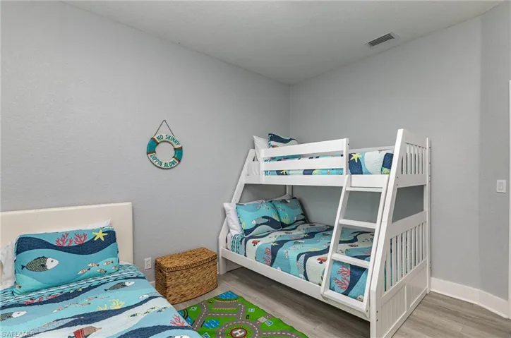 Bedroom featuring a white bunk bed frame with integrated ladder, a standalone bed with a white headboard, and wood-finish flooring