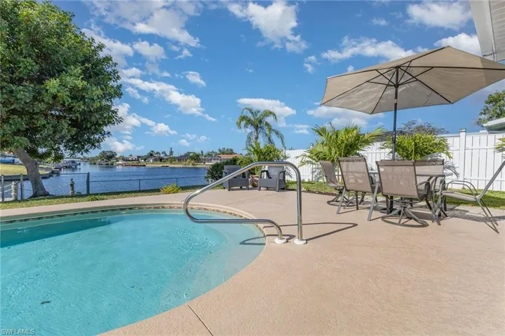 Curved swimming pool with a stainless steel handrail, surrounded by a concrete patio
