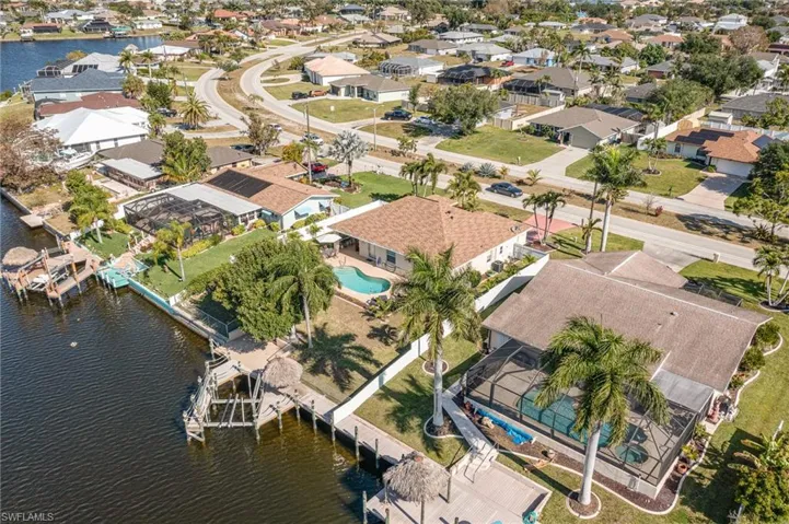 Waterfront property featuring a private dock, screened-in swimming pool, mature palm trees, and a manicured lawn