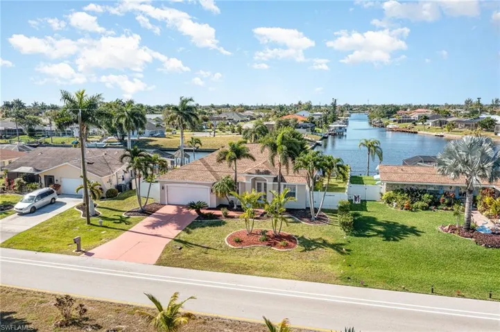 Waterfront property featuring a canal, mature palm trees, a well-maintained lawn, a paved driveway, and a white exterior