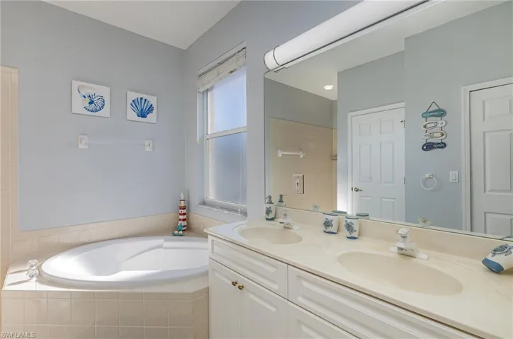 Spacious bathroom featuring a corner soaking tub with tiled surround, a large double vanity with integrated sinks, and a significant mirror with overhead lighting