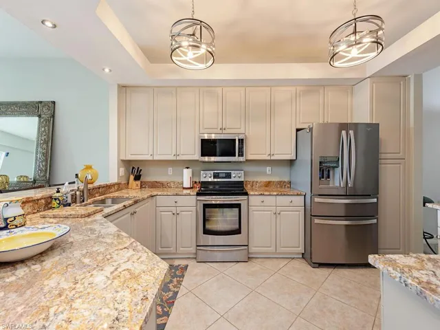 Kitchen with decorative light fixtures, light stone counters, a raised ceiling, appliances with stainless steel finishes, and light tile patterned floors