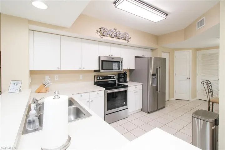 Kitchen featuring light tile patterned flooring, appliances with stainless steel finishes, and white cabinets