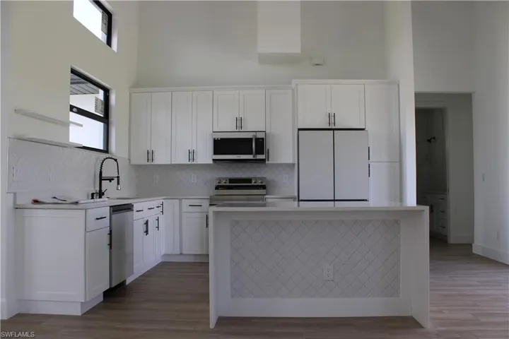 Kitchen with stainless steel appliances, a high ceiling, white cabinets, a center island, and light wood-style flooring