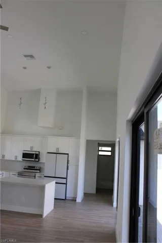 Kitchen featuring a high ceiling, range, stainless steel fridge, white cabinets, and decorative light fixtures