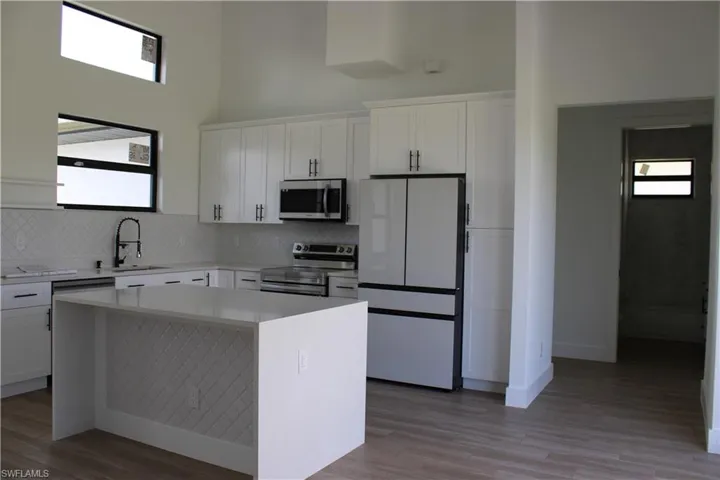 Kitchen featuring stainless steel appliances, white cabinetry, light wood-type flooring, light stone countertops, and a high ceiling