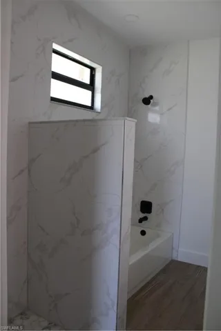 Bathroom with wood finished floors and a combined bath / shower with marble appearance