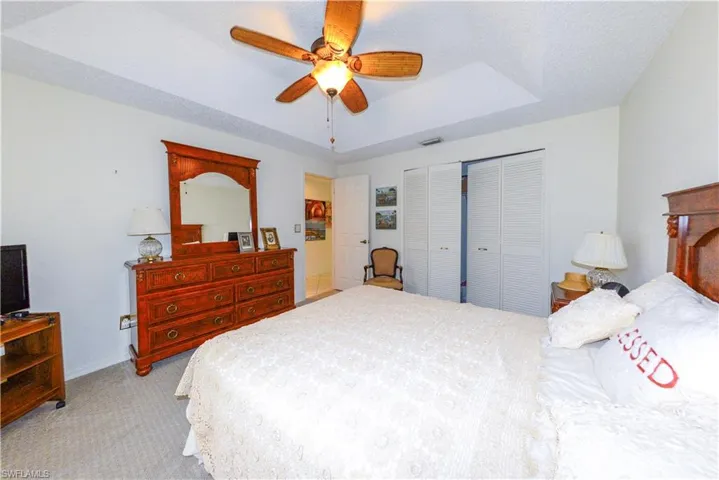 Bedroom with ceiling fan, light colored carpet, a tray ceiling, and a closet