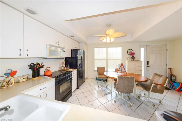 Kitchen featuring light tile patterned flooring, black appliances, white cabinetry, sink, and a tray ceiling