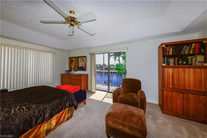 Bedroom featuring ceiling fan, a water view, a textured ceiling, access to outside, and light colored carpet