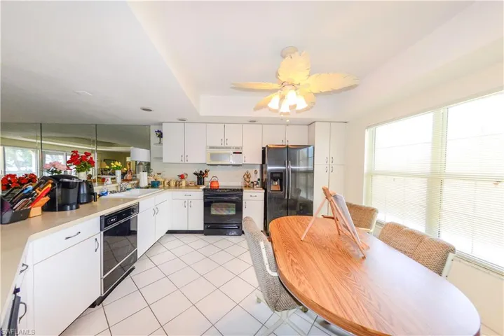 Kitchen with light tile patterned flooring, sink, black appliances, a tray ceiling, and white cabinets