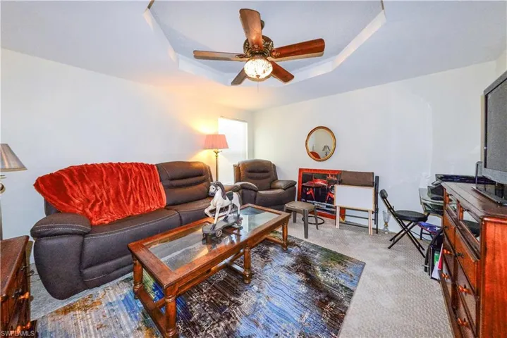 Living room with light carpet, a tray ceiling, and ceiling fan