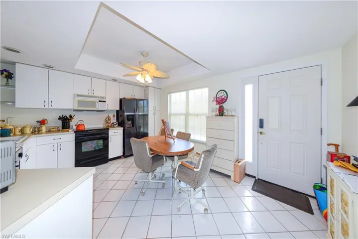 Kitchen featuring a raised ceiling, white cabinetry, light tile patterned floors, and black appliances