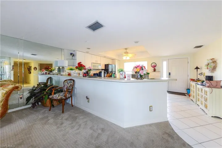 Kitchen with light tile patterned flooring, white cabinetry, ceiling fan, kitchen peninsula, and black fridge