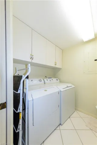 Laundry area featuring cabinets, light tile patterned flooring, electric panel, and independent washer and dryer