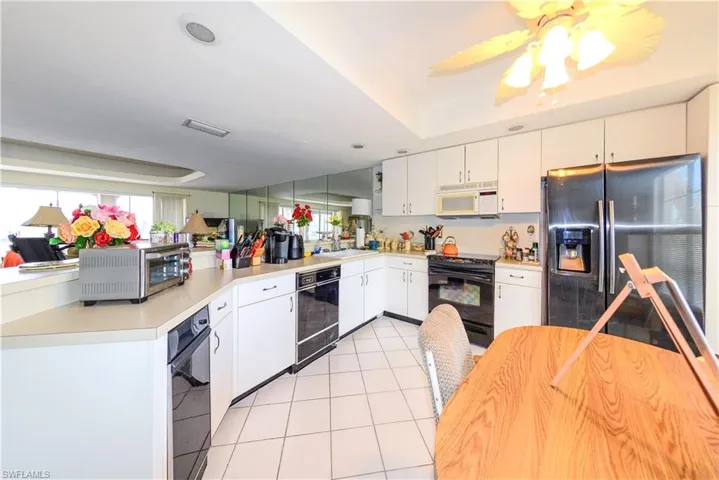 Kitchen with white cabinets, a wealth of natural light, light tile patterned floors, and black appliances