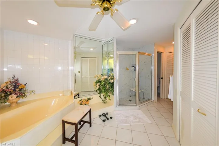 Bathroom featuring ceiling fan, tile patterned floors, separate shower and tub, and tile walls