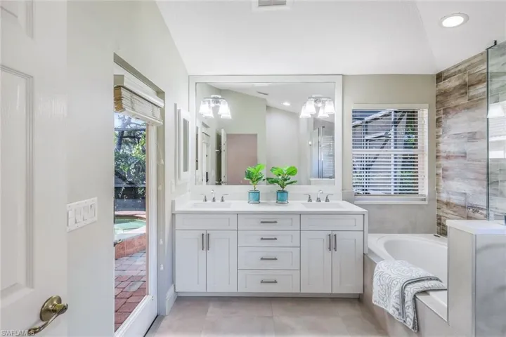 Bathroom with lofted ceiling, tile patterned floors, double sink vanity, and a washtub
