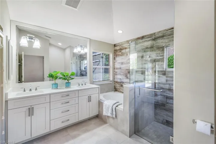 Bathroom with shower with separate bathtub, tile patterned flooring, lofted ceiling, and double sink vanity