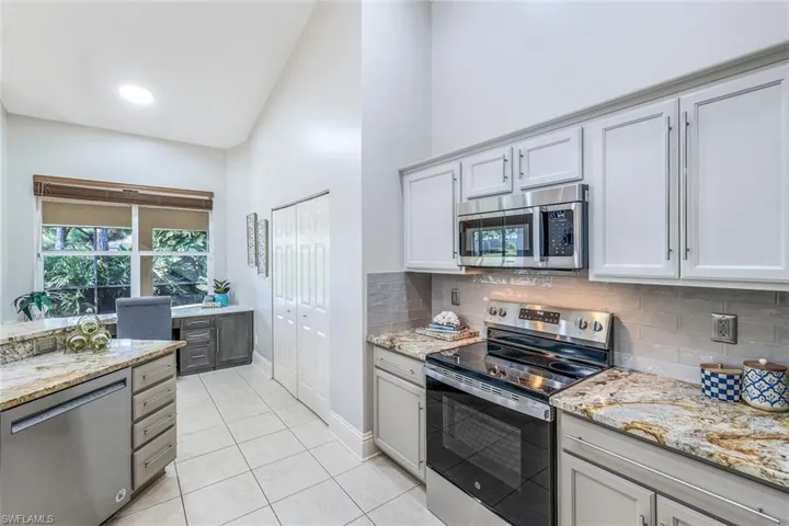 Kitchen featuring tasteful backsplash, white cabinets, stainless steel appliances, light stone counters, and light tile patterned floors