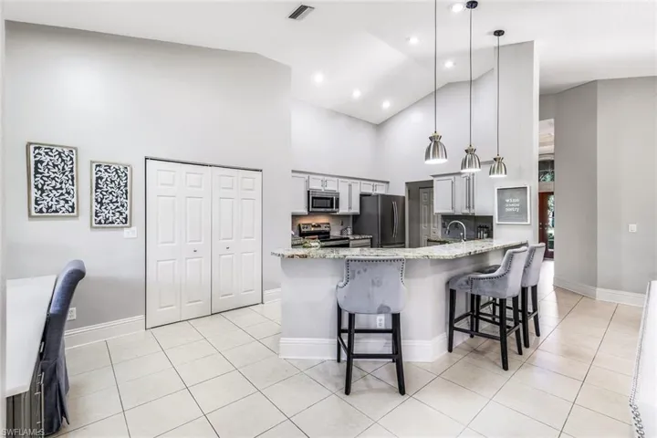 Kitchen featuring appliances with stainless steel finishes, kitchen peninsula, hanging light fixtures, light tile patterned flooring, and high vaulted ceiling