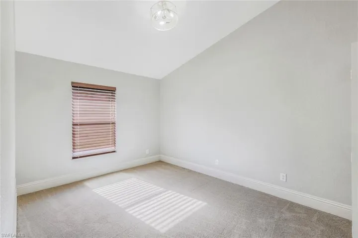 Carpeted spare room featuring vaulted ceiling