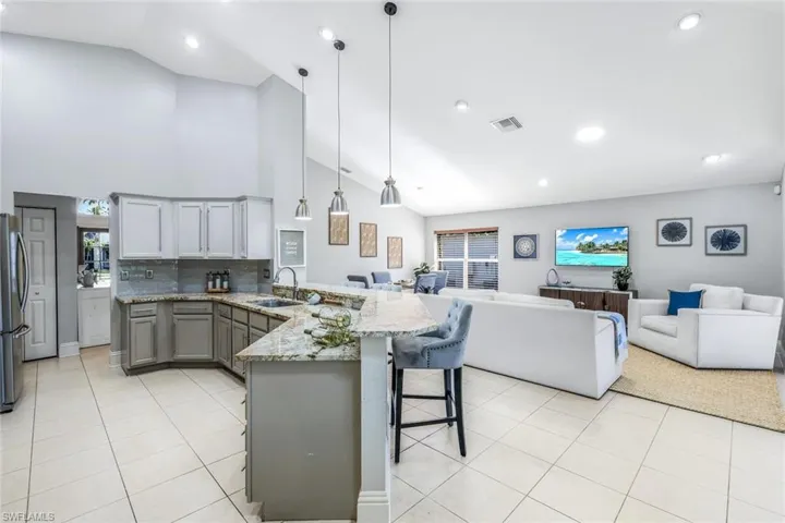 Kitchen featuring a kitchen bar, gray cabinetry, kitchen peninsula, hanging light fixtures, and light stone countertops