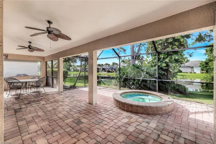 View of patio featuring an in ground hot tub, a water view, ceiling fan, and a lanai