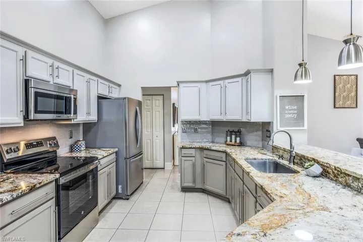 Kitchen featuring light tile patterned flooring, backsplash, appliances with stainless steel finishes, sink, and high vaulted ceiling