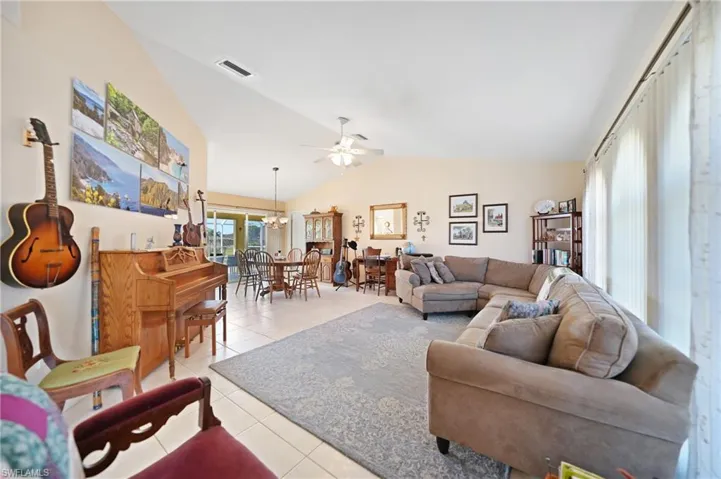 Tiled living room featuring lofted ceiling and ceiling fan with notable chandelier