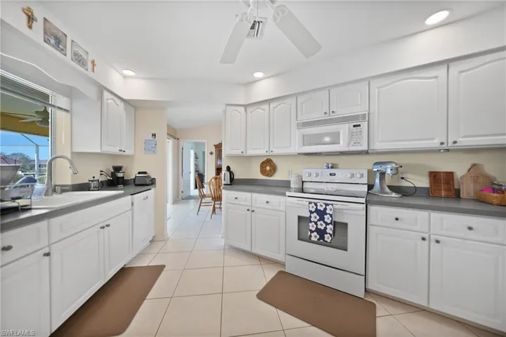 Kitchen with light tile patterned flooring, white cabinetry, sink, ceiling fan, and white appliances