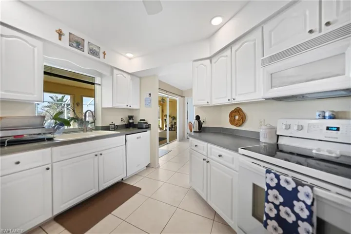 Kitchen featuring light tile patterned flooring, white appliances, sink, and white cabinets