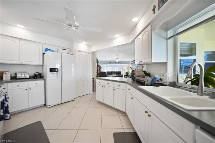 Kitchen with sink, white refrigerator with ice dispenser, white cabinets, and ceiling fan