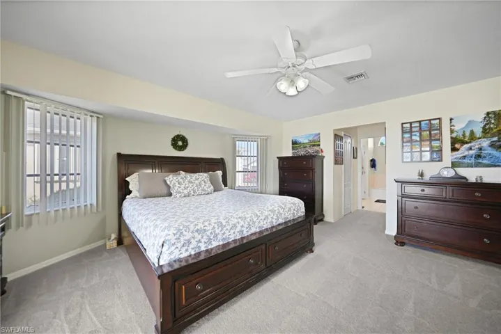 Bedroom with ceiling fan, connected bathroom, and light colored carpet