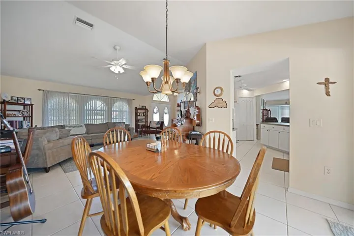 Dining space with light tile patterned floors, ceiling fan with notable chandelier, and vaulted ceiling