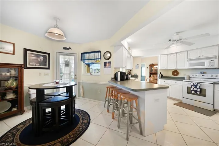 Kitchen featuring a breakfast bar, white cabinetry, light tile patterned floors, kitchen peninsula, and white appliances