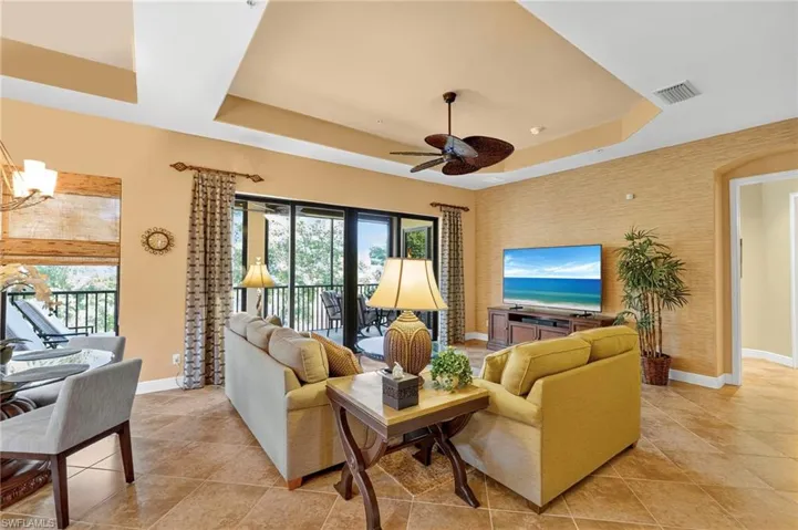 Living area with a tray ceiling, light tile patterned floors, a chandelier, and ceiling fan