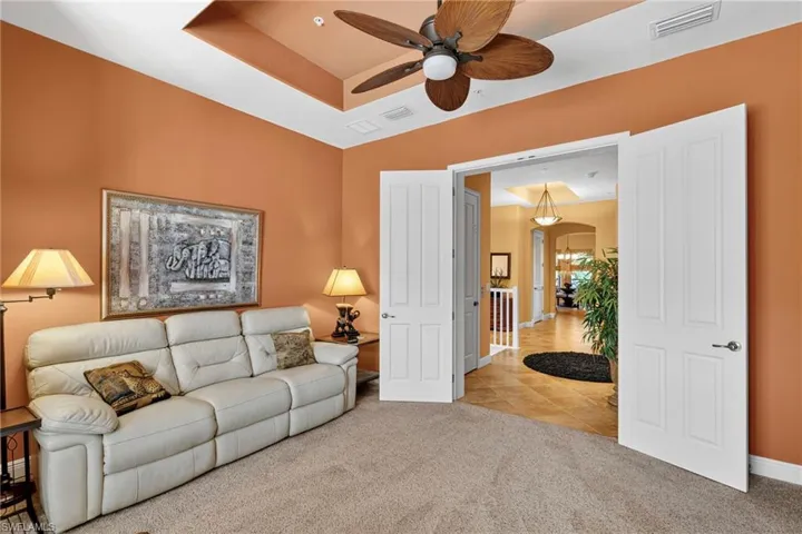 Tiled living room with a tray ceiling, carpet floors, a ceiling fan, and arched walkways