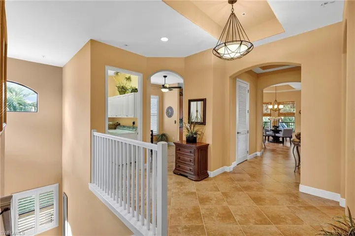 Corridor with arched walkways, a chandelier, recessed lighting, light tile patterned floors, and a raised ceiling